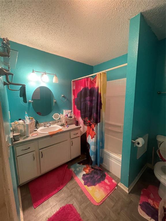 full bathroom featuring toilet, vanity, shower / bathtub combination with curtain, and a textured ceiling