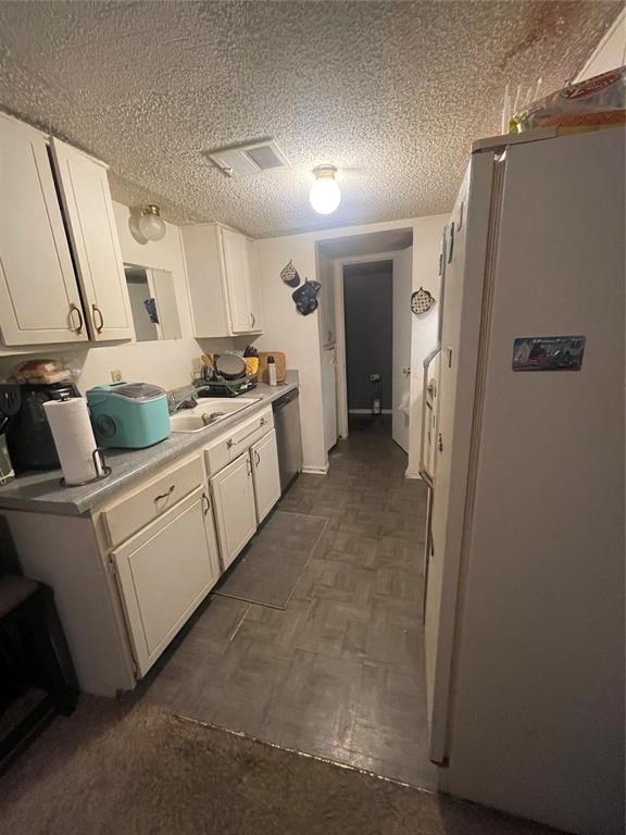 kitchen featuring sink, white cabinetry, a textured ceiling, stainless steel dishwasher, and white fridge