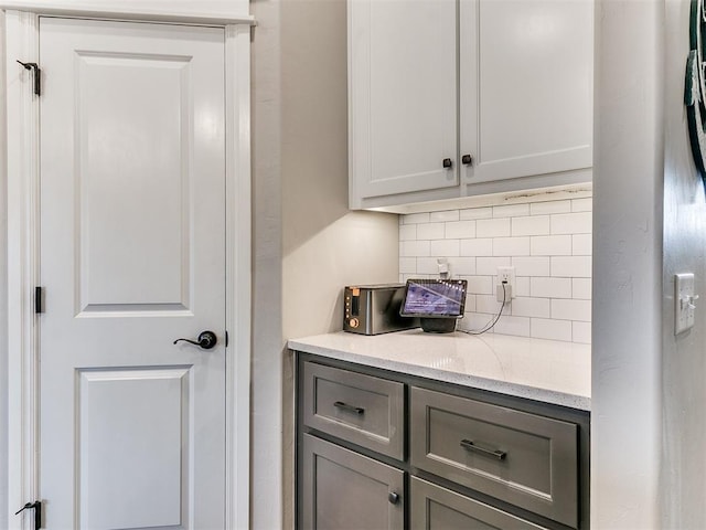 bar with backsplash, light stone counters, and gray cabinetry