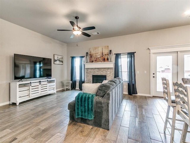 living room featuring hardwood / wood-style flooring, a stone fireplace, and ceiling fan