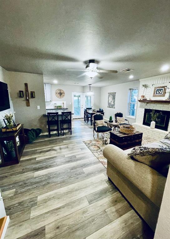 living room featuring a fireplace, a textured ceiling, light hardwood / wood-style floors, and ceiling fan