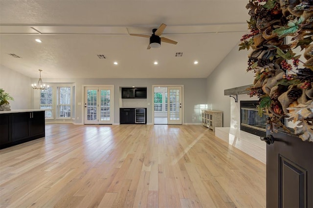 unfurnished living room featuring a textured ceiling, lofted ceiling, ceiling fan with notable chandelier, and light wood-type flooring