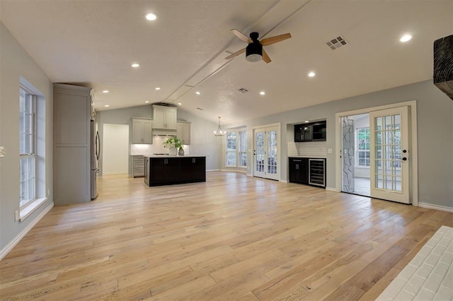 unfurnished living room with ceiling fan with notable chandelier, light wood-type flooring, vaulted ceiling, and a wealth of natural light