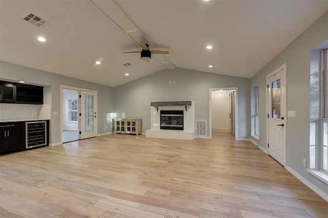 unfurnished living room with ceiling fan, beverage cooler, lofted ceiling, and light wood-type flooring