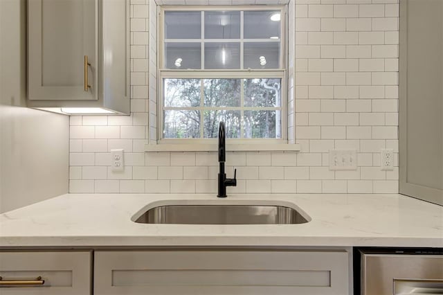 kitchen featuring backsplash, light stone counters, and sink