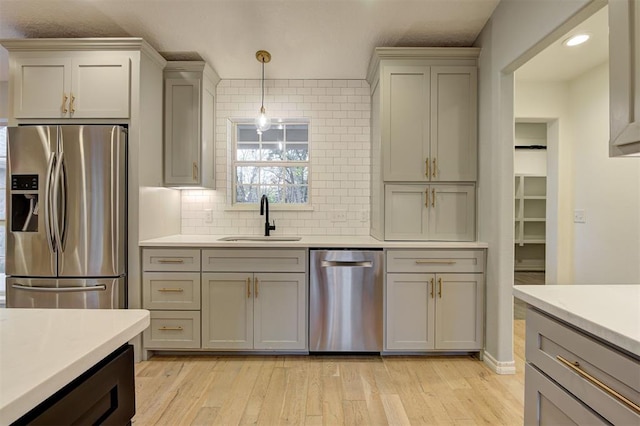 kitchen with appliances with stainless steel finishes, light hardwood / wood-style flooring, hanging light fixtures, and sink