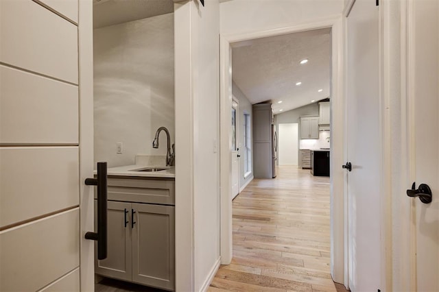 hall featuring sink, vaulted ceiling, and light wood-type flooring