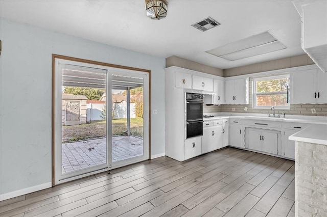 kitchen featuring sink, light wood-type flooring, white cabinetry, and backsplash