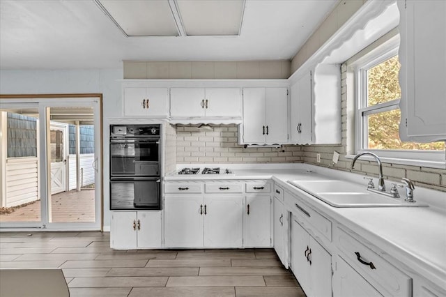 kitchen with light wood-type flooring, black double oven, white gas cooktop, sink, and white cabinetry