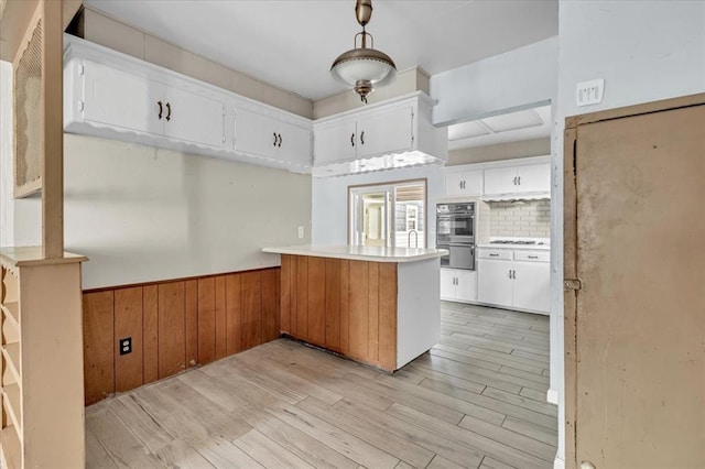 kitchen featuring wood walls, kitchen peninsula, light hardwood / wood-style flooring, tasteful backsplash, and white cabinetry