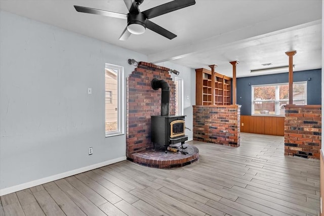 living room featuring a wood stove, ceiling fan, a healthy amount of sunlight, and light wood-type flooring