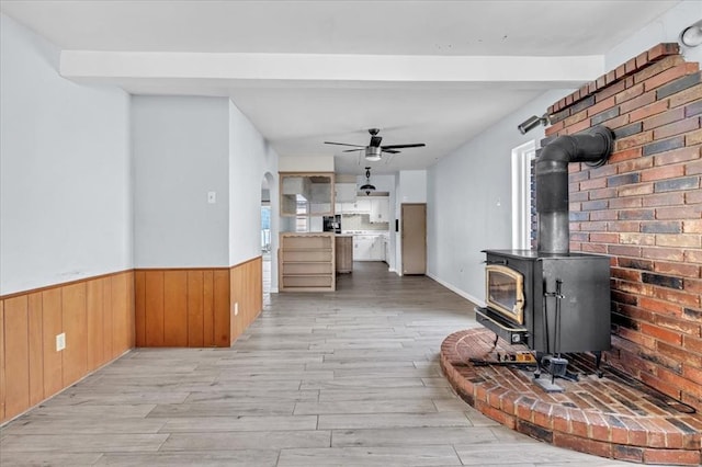 living room with light hardwood / wood-style flooring, a wood stove, ceiling fan, and brick wall