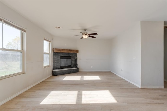 unfurnished living room with ceiling fan, a stone fireplace, and light wood-type flooring