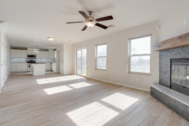 unfurnished living room featuring a fireplace, light hardwood / wood-style floors, and ceiling fan