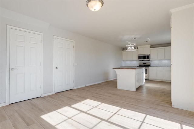 kitchen with a center island, appliances with stainless steel finishes, decorative backsplash, white cabinets, and light wood-type flooring