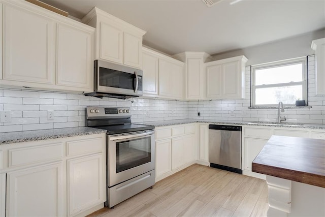 kitchen with white cabinetry, sink, light hardwood / wood-style floors, decorative backsplash, and appliances with stainless steel finishes