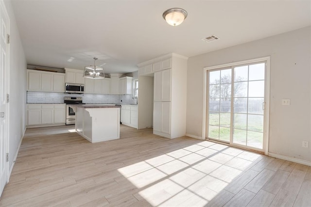 kitchen featuring decorative backsplash, appliances with stainless steel finishes, light wood-type flooring, a center island, and white cabinetry