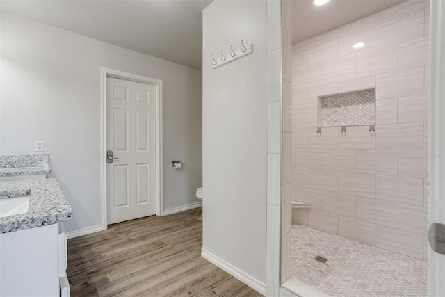 bathroom featuring tiled shower, toilet, vanity, and hardwood / wood-style flooring