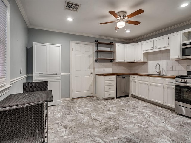 kitchen with white cabinets, sink, ceiling fan, ornamental molding, and stainless steel appliances