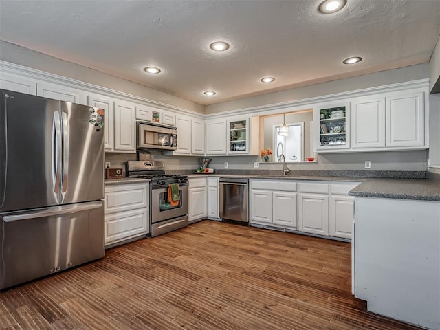 kitchen featuring appliances with stainless steel finishes, sink, pendant lighting, white cabinets, and hardwood / wood-style floors