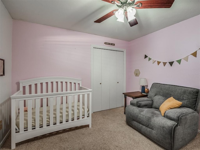 bedroom with ceiling fan, a closet, light colored carpet, and a nursery area