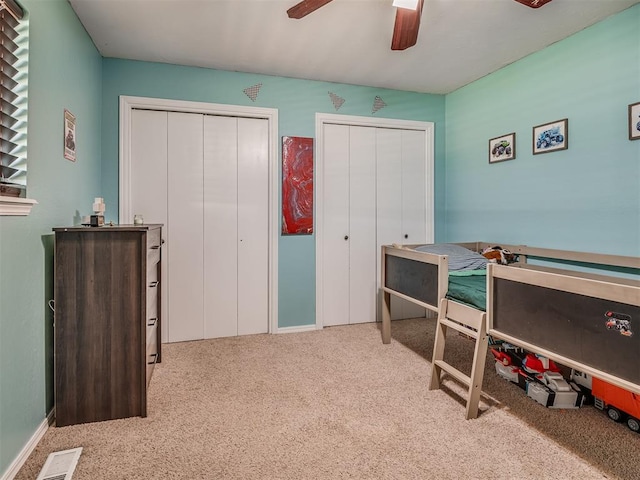 carpeted bedroom with ceiling fan and multiple closets