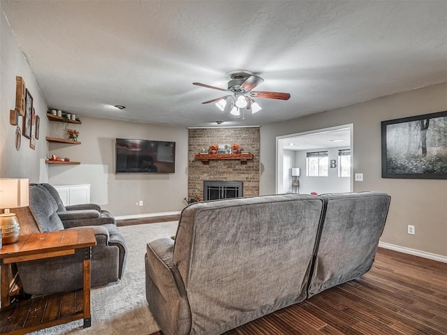 living room featuring a fireplace, a textured ceiling, ceiling fan, and dark wood-type flooring