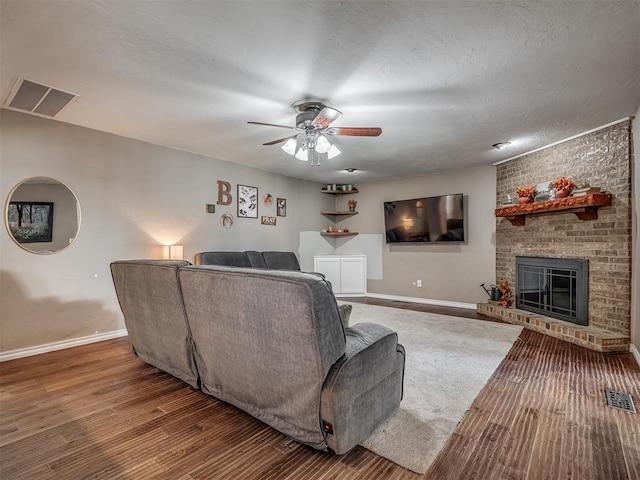 living room with ceiling fan, a fireplace, wood-type flooring, and a textured ceiling