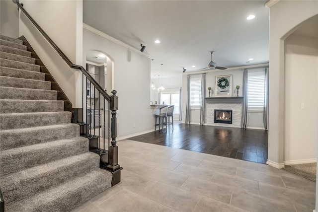 unfurnished living room featuring a stone fireplace, ornamental molding, ceiling fan, and tile patterned floors