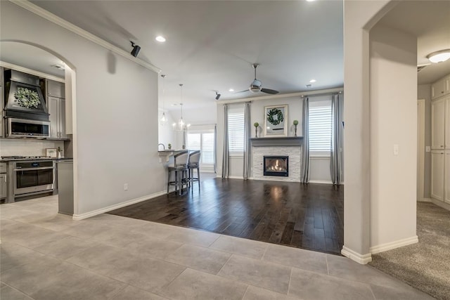 living room with crown molding, a stone fireplace, and ceiling fan