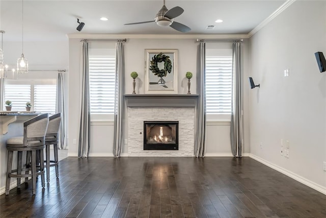 living room with dark hardwood / wood-style flooring, crown molding, a stone fireplace, and ceiling fan