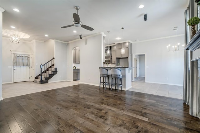 unfurnished living room with ornamental molding, ceiling fan with notable chandelier, and dark hardwood / wood-style flooring