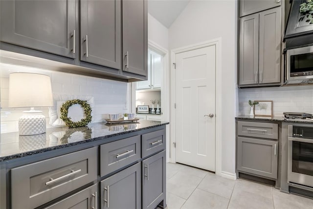 kitchen featuring gray cabinets, lofted ceiling, dark stone countertops, light tile patterned floors, and stainless steel appliances