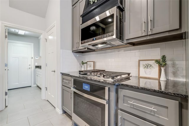 kitchen featuring stainless steel appliances, gray cabinets, dark stone countertops, and decorative backsplash