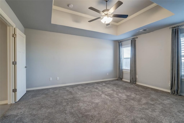 spare room featuring a raised ceiling, dark colored carpet, and ceiling fan