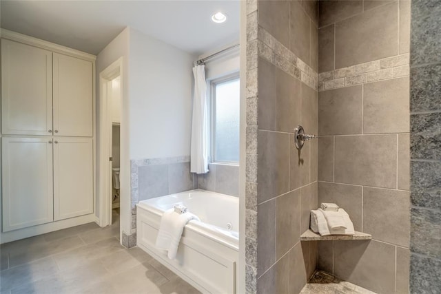 bathroom with tile patterned floors, a tub to relax in, toilet, and tile walls