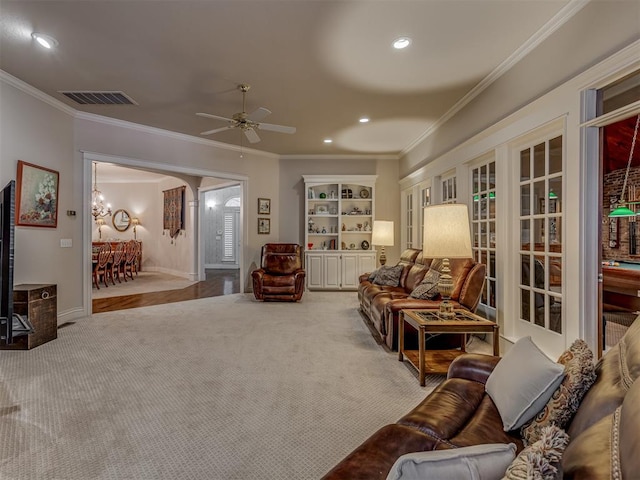 carpeted living room featuring crown molding and ceiling fan with notable chandelier