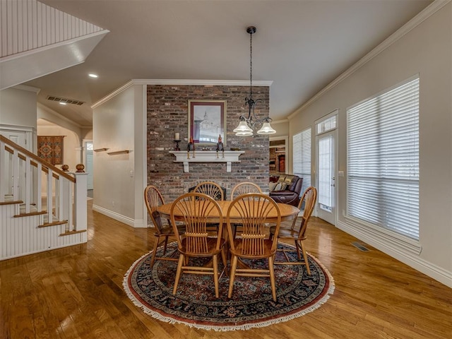 dining room featuring crown molding, wood-type flooring, and a brick fireplace