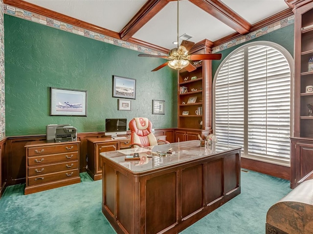 home office with built in features, beamed ceiling, ornamental molding, ceiling fan, and light carpet