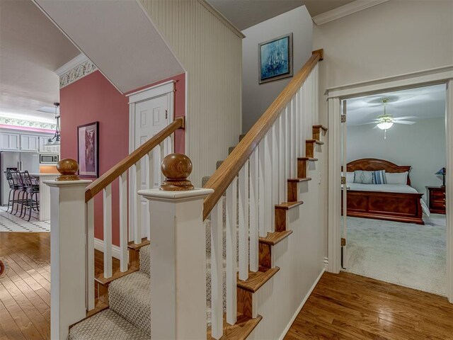 stairway with crown molding, ceiling fan, and wood-type flooring