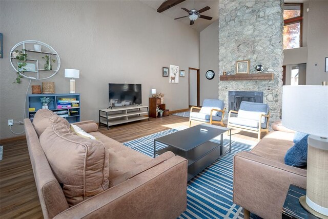 living room with hardwood / wood-style floors, high vaulted ceiling, a stone fireplace, ceiling fan, and beamed ceiling