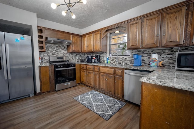 kitchen featuring appliances with stainless steel finishes, dark hardwood / wood-style flooring, ventilation hood, sink, and a notable chandelier