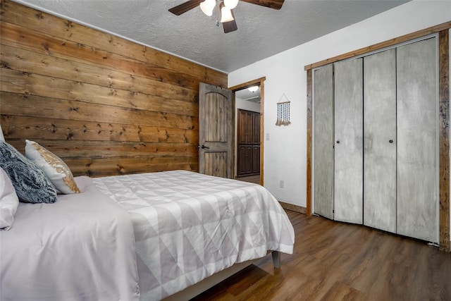 bedroom featuring a textured ceiling, dark hardwood / wood-style flooring, ceiling fan, and wood walls