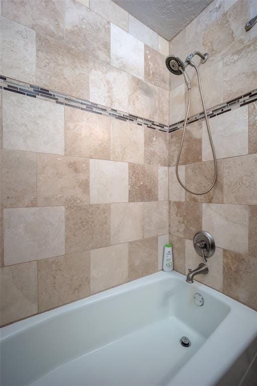 bathroom featuring a textured ceiling and tiled shower / bath