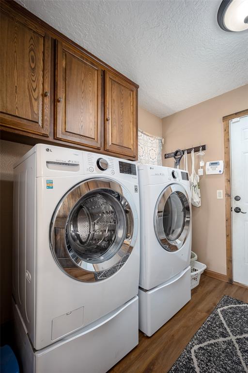 washroom with cabinets, a textured ceiling, washing machine and dryer, and dark hardwood / wood-style floors