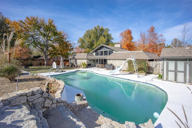 view of swimming pool with a storage shed, a patio, and a water slide