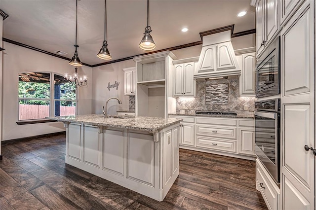 kitchen with light stone countertops, white cabinetry, stainless steel appliances, an island with sink, and pendant lighting