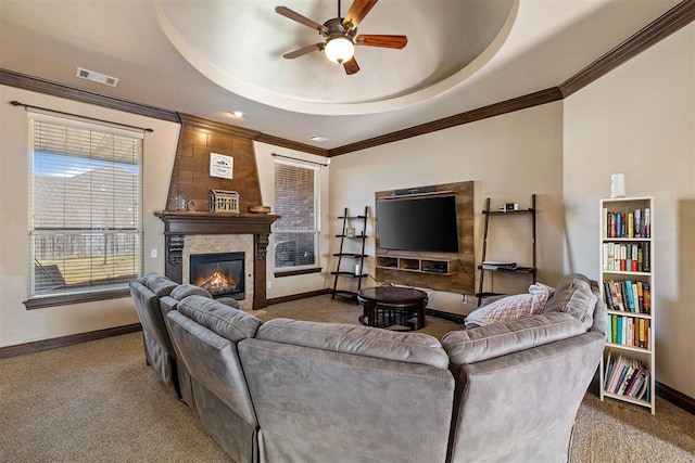 carpeted living room with a raised ceiling, ceiling fan, a fireplace, and crown molding