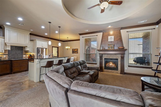 living room featuring a raised ceiling, sink, ceiling fan, ornamental molding, and a fireplace