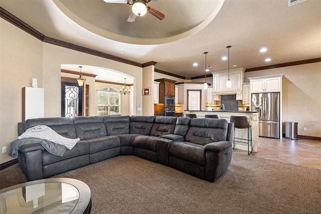 living room featuring sink, ceiling fan with notable chandelier, a raised ceiling, and crown molding